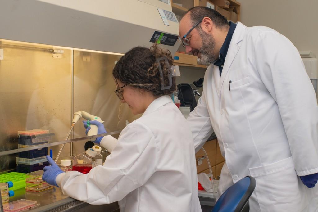 A professor watches over a student as they work with lab equipment